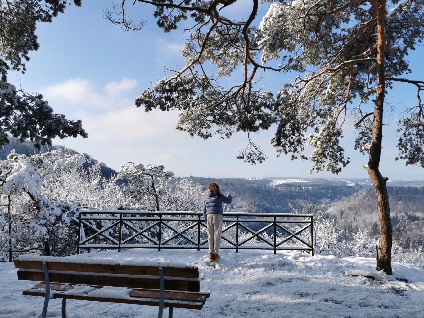 A snowy viewpoint with a bench and railing at Plateau Ruetsbech in Berdorf.