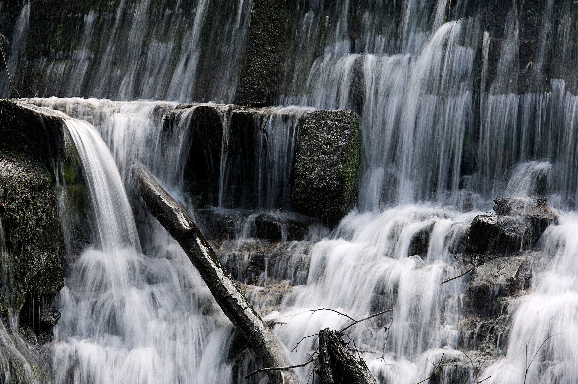 Gelaagde waterval met met mos begroeide rotsen en stromend water.