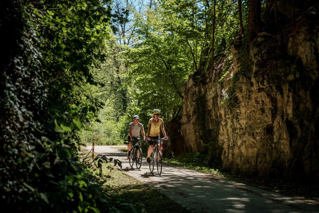 Two cyclists riding along a scenic path surrounded by greenery and rocky cliffs