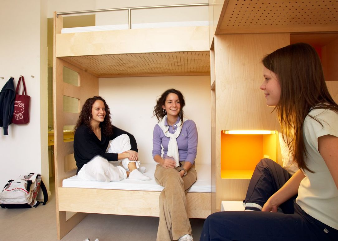Drie vriendinnen zitten op het bed in de jeugdherberg en praten.