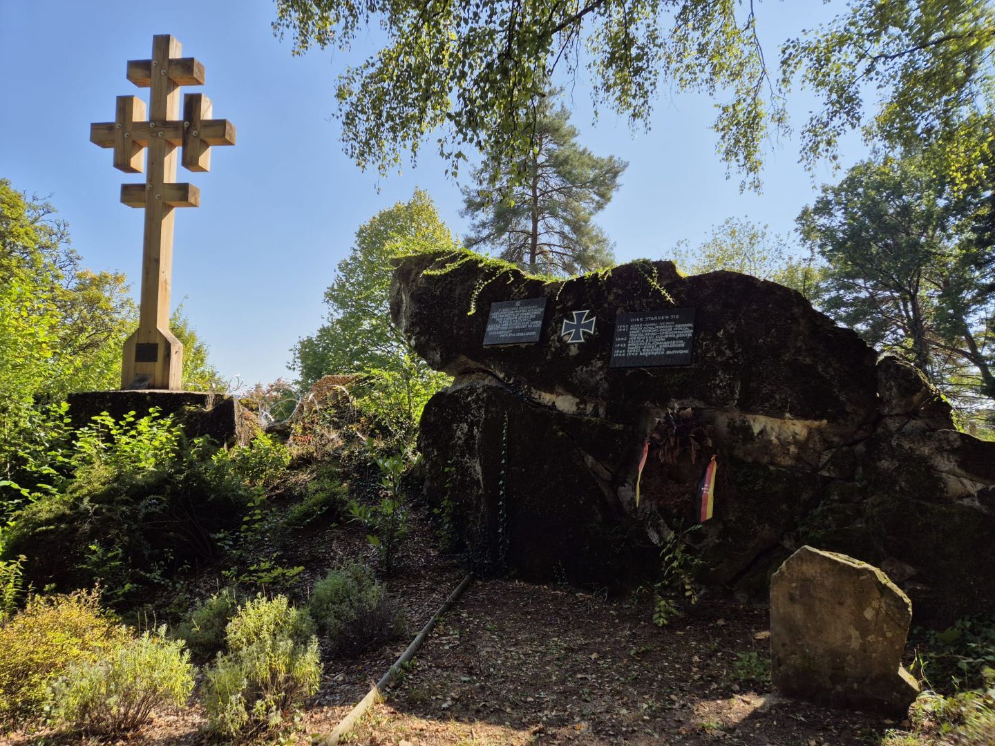Memorial site at the Katzenkopf Bunker in the Mullerthal Region with memorial cross and rock bunkers, surrounded by trees.