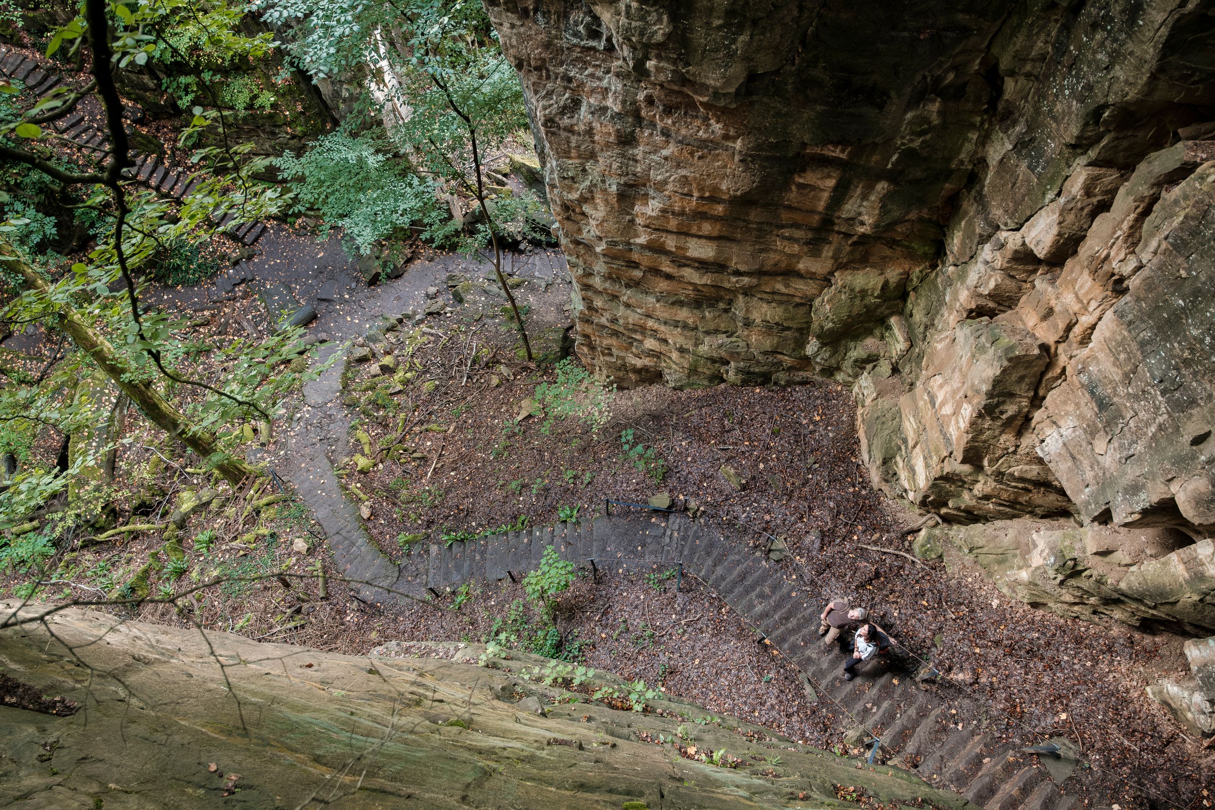 Zwei Wanderer steigen die steilen Steinstufen der „Wollefsschlucht“ in Echternach hinauf.