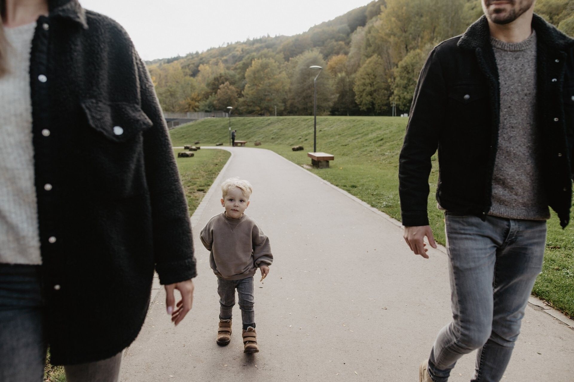 Jong kind wandelt tussen ouders op een pad in het groen.