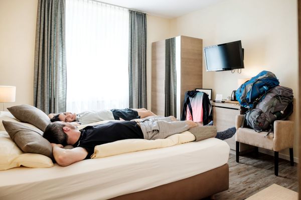 Two people resting briefly on the bed in their hotel room