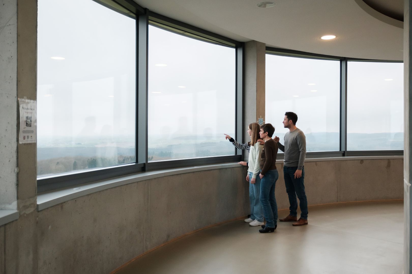 Vier personen kijken door grote ramen naar het landschap in de Aquatower in Berdorf.