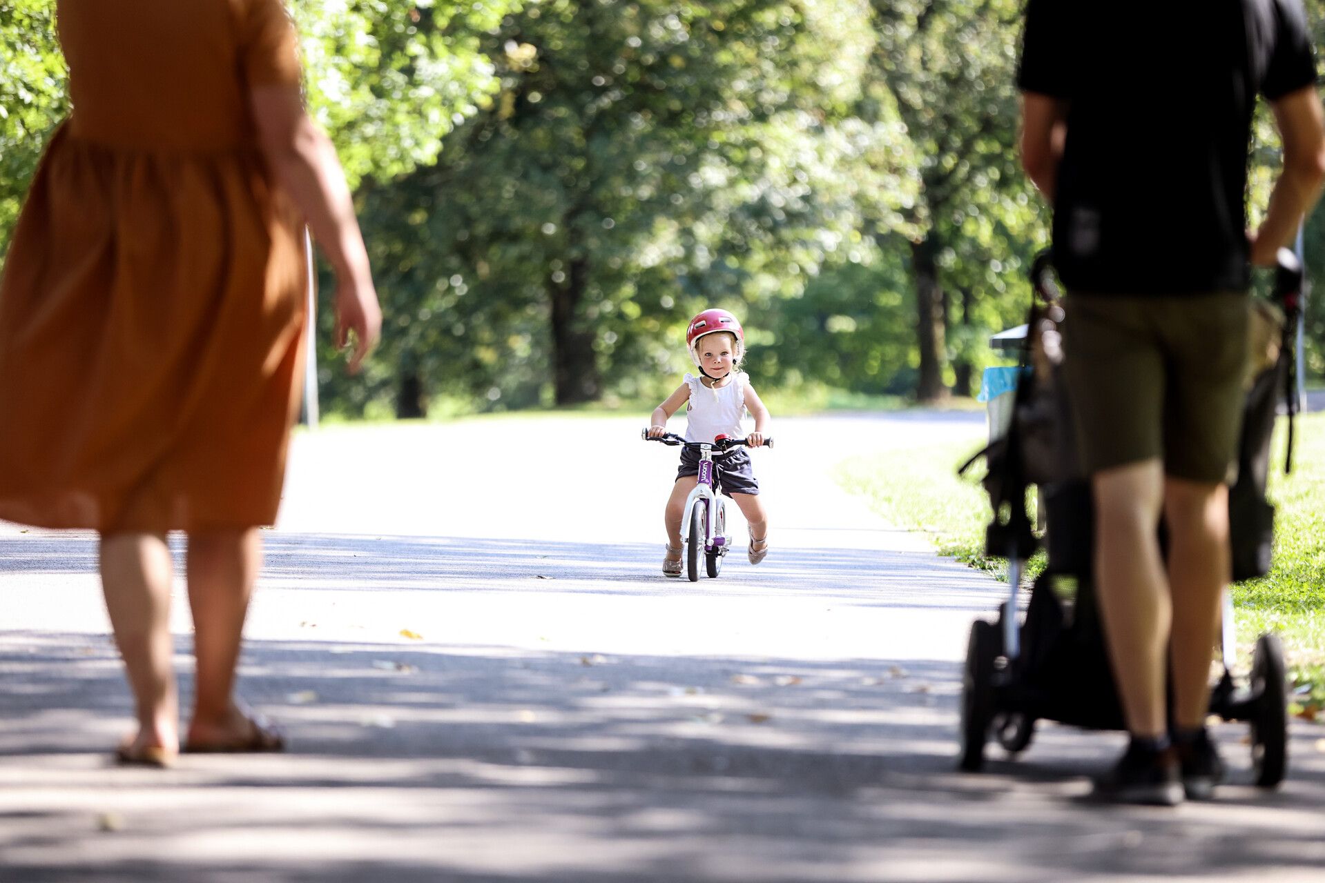 Enfant fait de la draisienne sur un chemin ensoleillé, parents au premier plan.