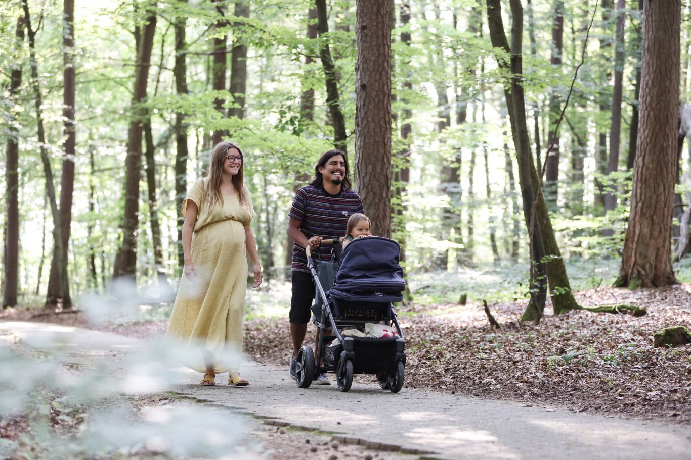 Familie mit Kinderwagen spaziert auf einem Waldweg im Frühling.