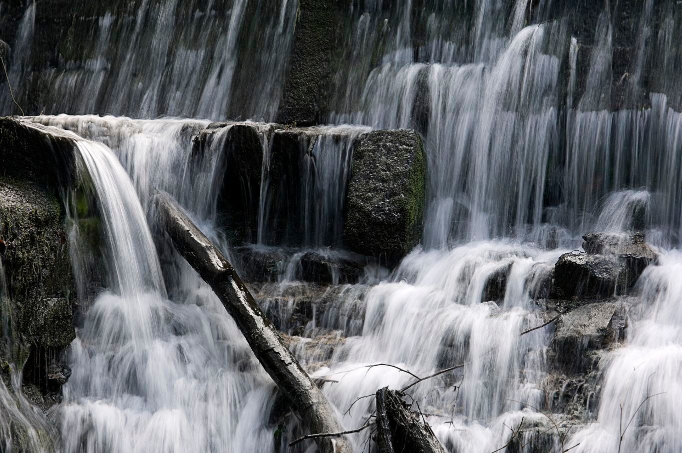 Stufiger Wasserfall mit moosbedeckten Felsen und fließendem Wasser.