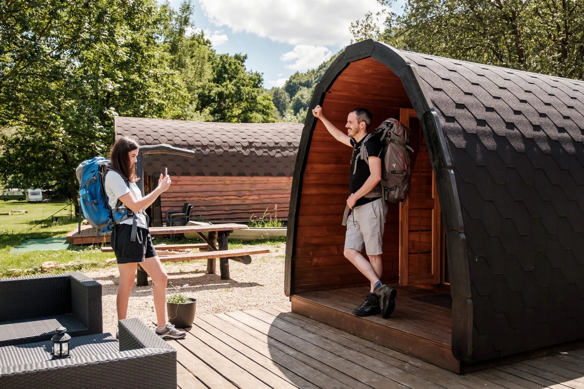 Twee personen voor hun campingpod, de vrouw fotografeert de man