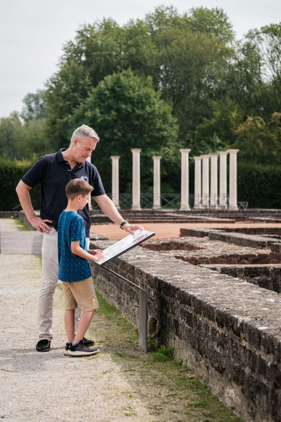 Een vader en zijn zoon lezen samen het informatiebord bij de Romeinse villa in Echternach.