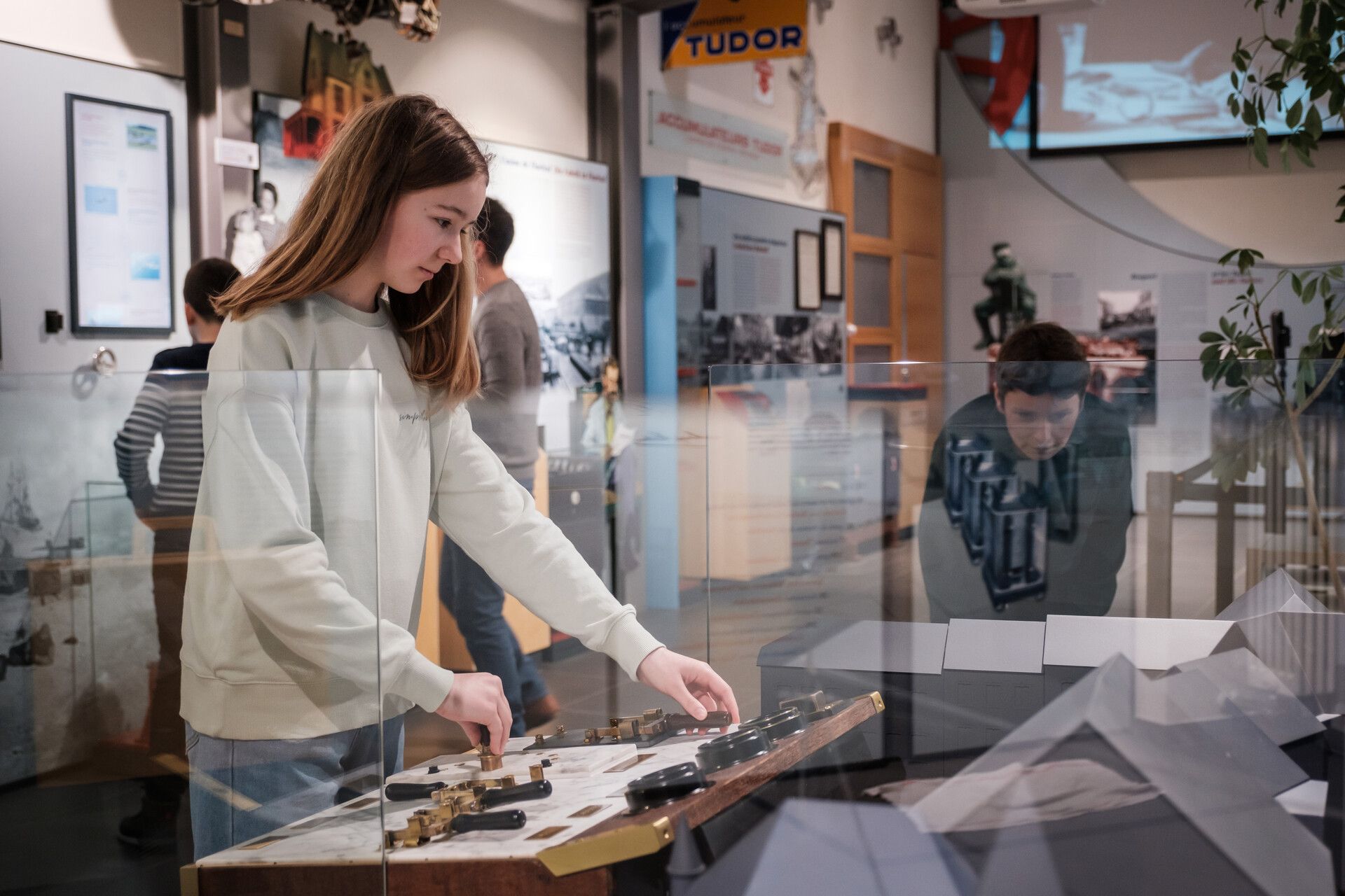 Girl exploring an interactive station in the museum, mother in the background.