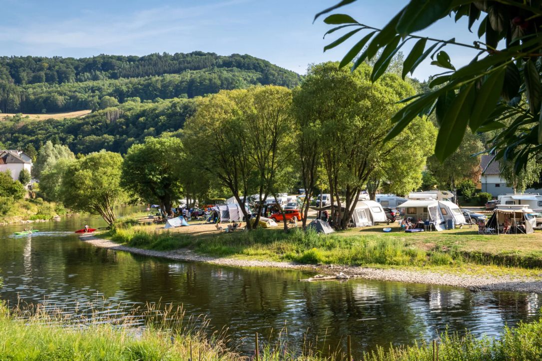 Camping aan de rivier, omgeven door bomen en heuvels op een zonnige dag.